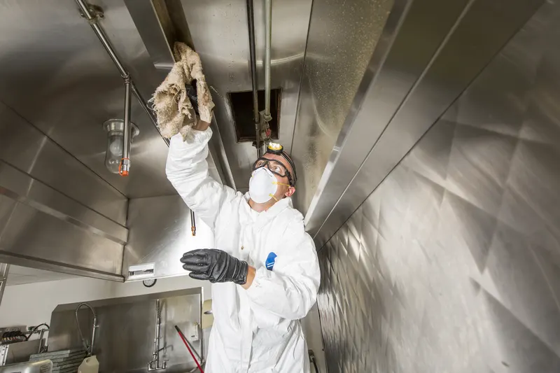 Gloved hand wiping grease from the plenum behind the filter bank inside a commercial kitchen hood